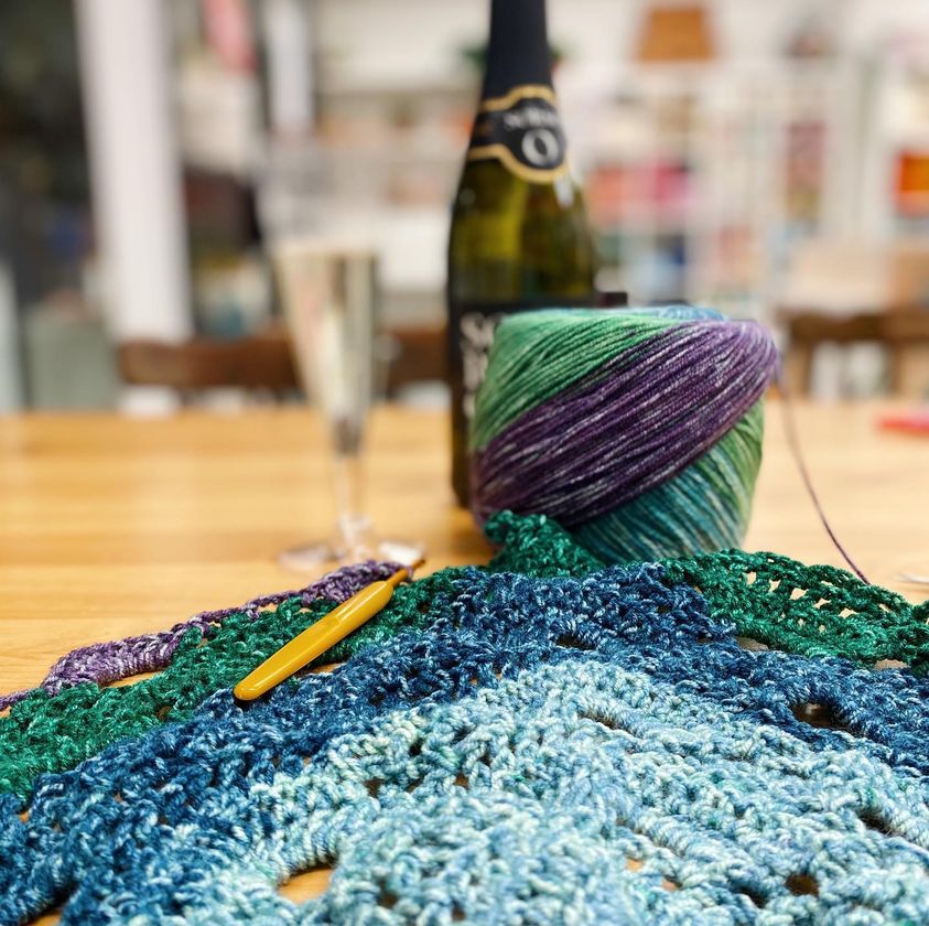 Woolly Wednesday craft group depicted by a ball of wool yarn and a bottle of Prosecco in the background