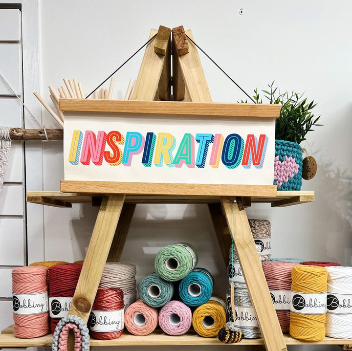 board with the word inspiration on it and coloured yarns on the bench below